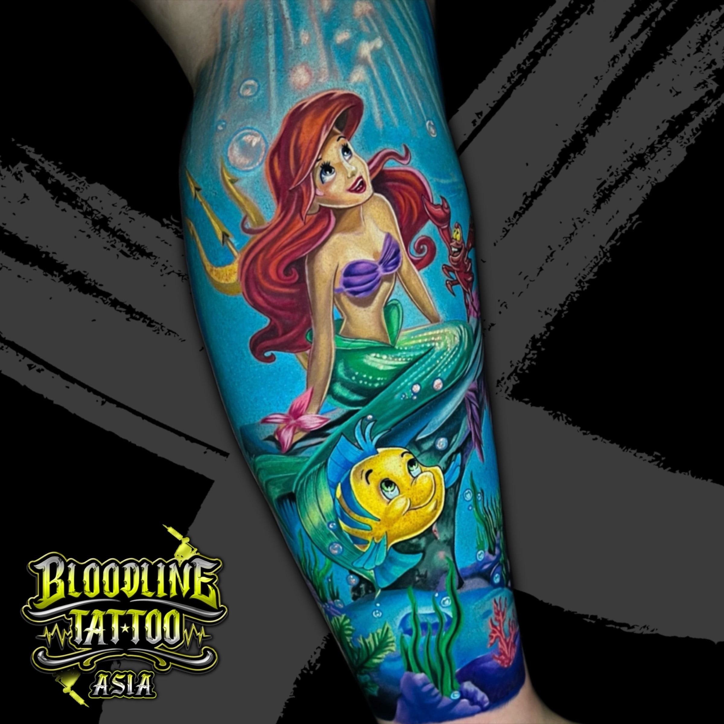 Colour illustrative forearm tattoo of Ariel, Flounder, and Sebastian from The Little Mermaid underwater at Bloodline Tattoo Bali.