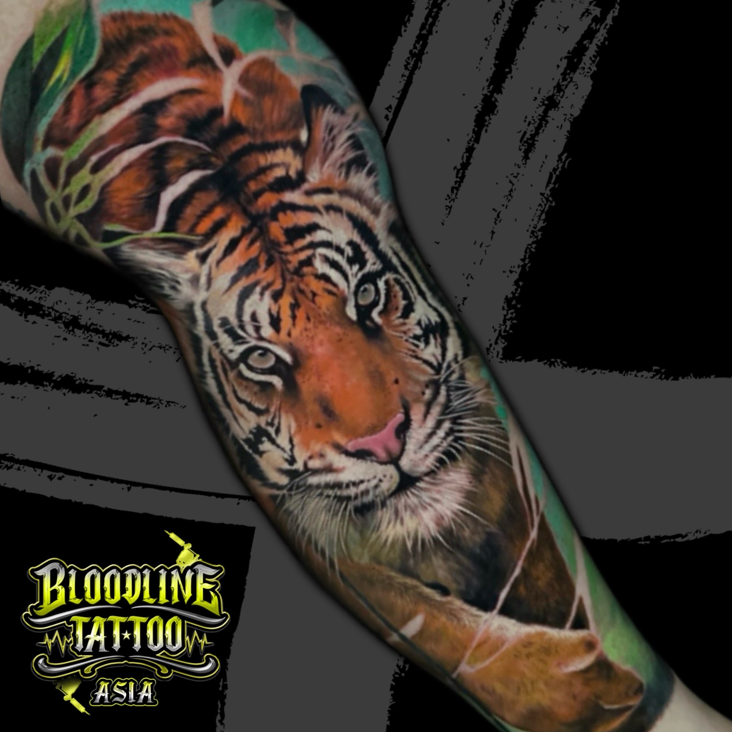 Colour realistic forearm tattoo of a tiger's face with orange fur, black stripes, and green foliage at Bloodline Tattoo Bali.