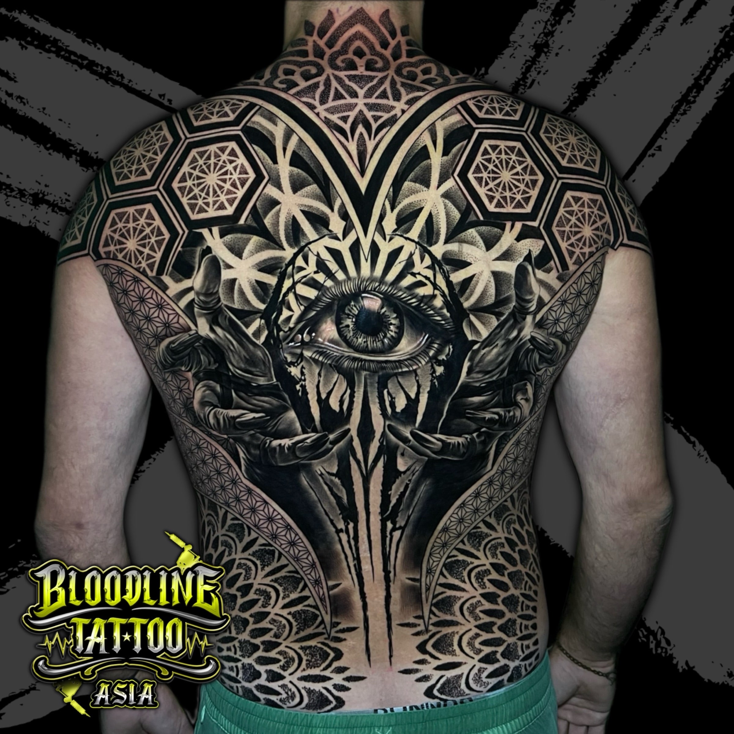 Full-back tattoo with realistic central eye framed by shadowed hands, upper mandala, and hexagonal Flower of Life panels in dense dotwork, at Bloodline Tattoo Bali.